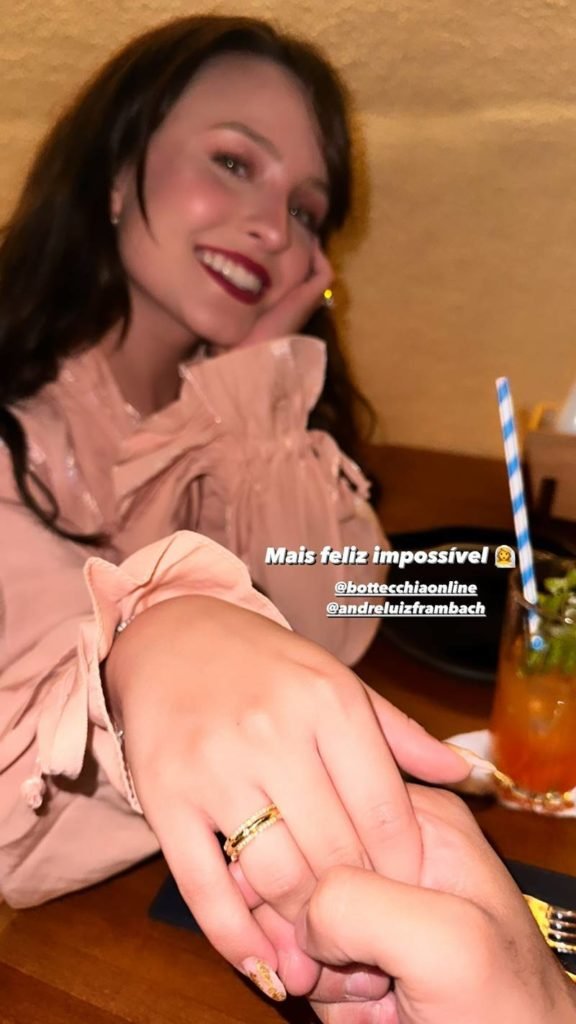 Larissa Manoela sentada em mesa de blusa rosa mostra mão com aliança - metrópoles