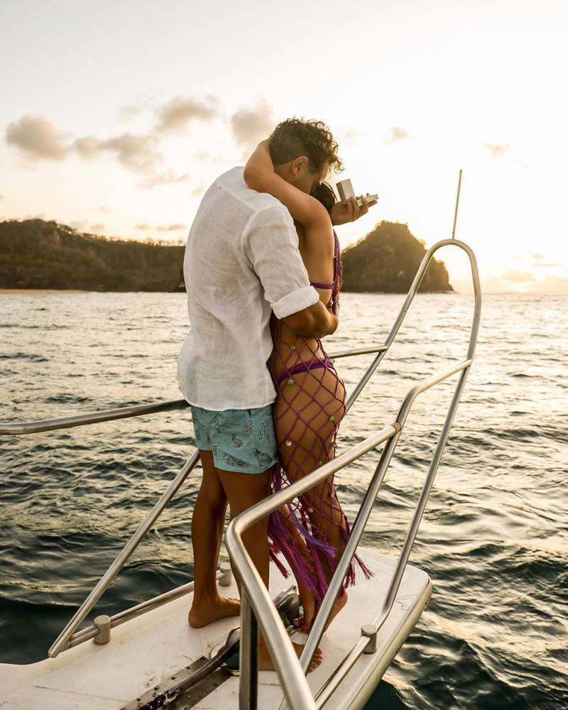 Larissa Manoela e André Luiz Frambach abraçados na ponta de um barco com mar ao fundo - metrópoles