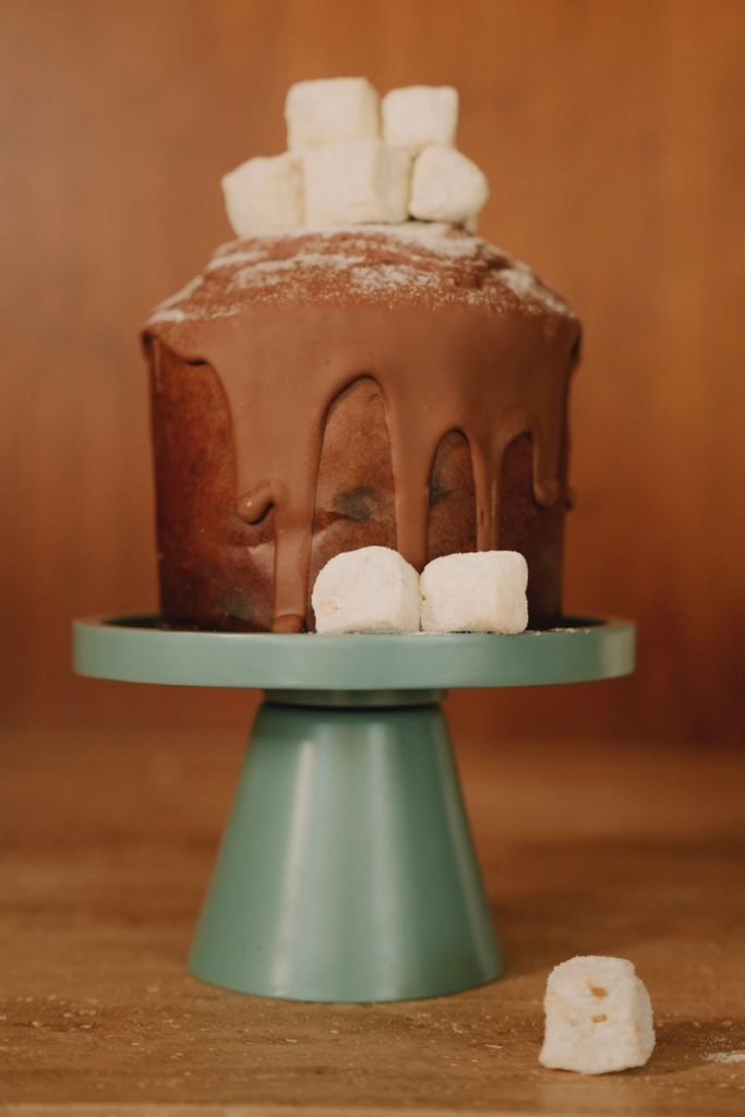 Foto colorida de chocotone com marshmallow no topo e ao redor. Os doces estão em uma bandeja verde - Metrópoles