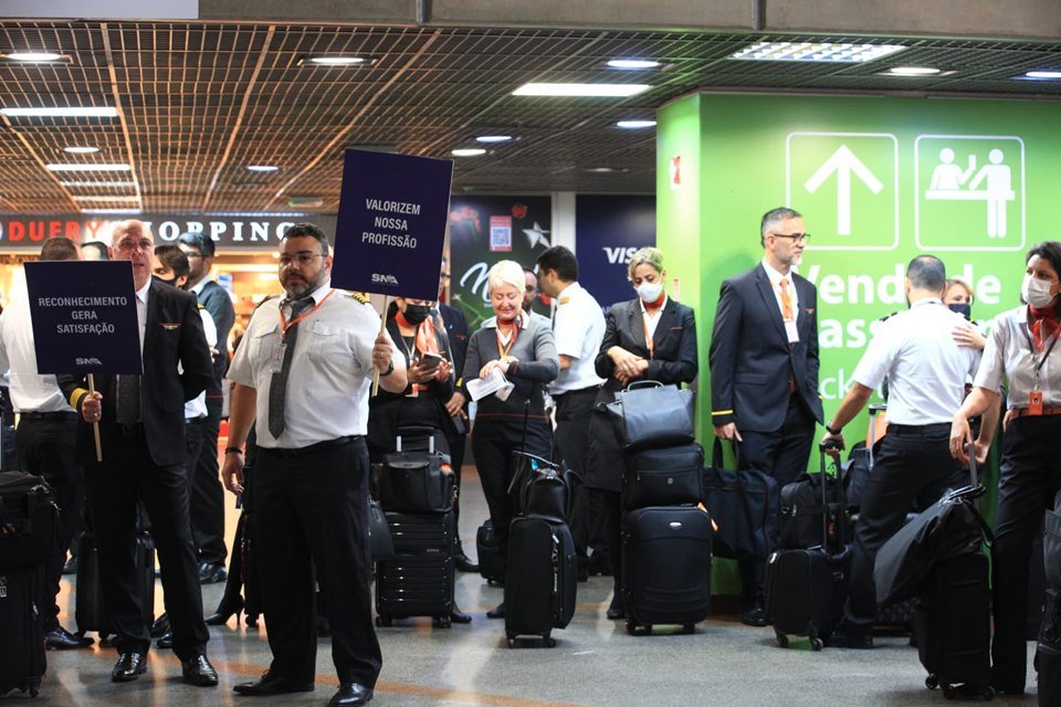 Grupo de pessoas reunido no Aeroporto de Brasília, para segundo dia de paralisação dos aeronautas. Próximos aos manifestantes, que usam uniformes e seguram placas, há passageiros com malas - Metrópoles
