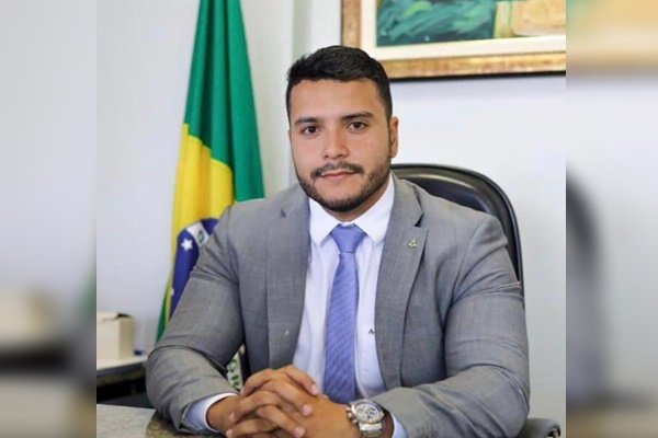 Gustavo Amaral, anunciado como secretário da Ciência e Tecnologia no novo governo Ibaneis. Ele olha para a câmera sentado à mesa diante de uma bandeira do Brasil - Metrópoles