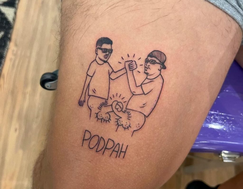 Apresentadores do PodPah, Igão e Mitico tatuam os próprios pênis entrelaçados. No detalhe, um deles posa para foto ao lado da coxa do outro - Metrópoles