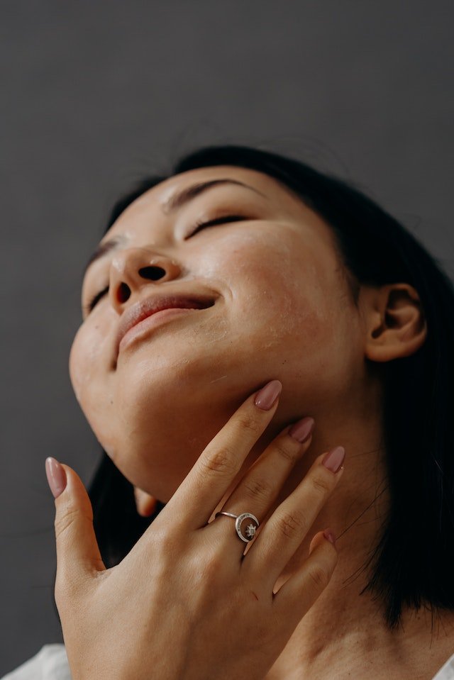 Rosto de mulher jovem asiática sorrindo com a mão no pescoço - Metrópoles