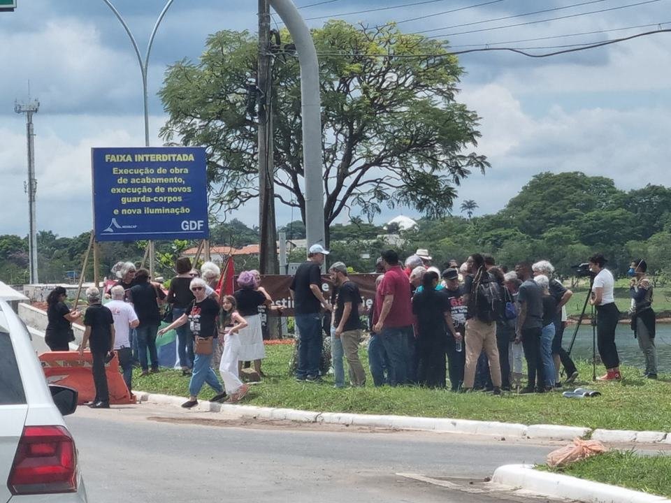 Pessoas em gramado ao lado de placa em dia nublado