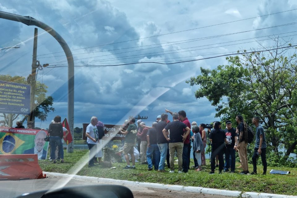 Pessoas em gramado ao lado de placa em dia nublado