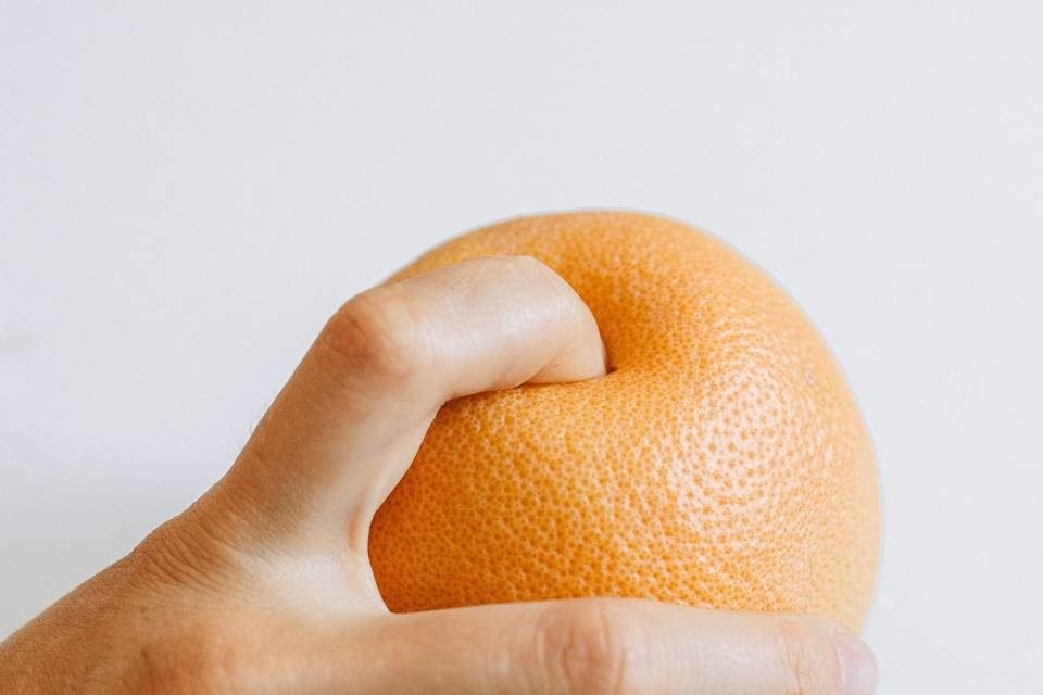 Pessoa enfiando o dedo em uma laranja - Metrópoles