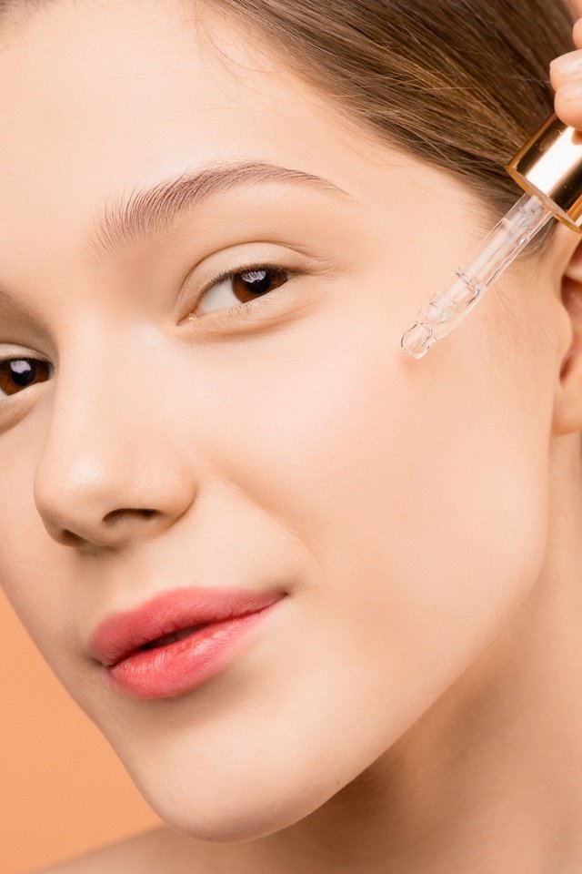 Rosto de mulher branca aplicando óleo facial - Metrópoles