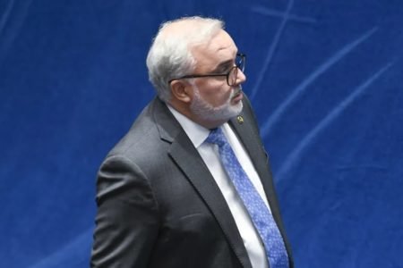 O ex-senador Jean Paul Prates, atual presidente da Petrobras, usa terno e caminha sobre um fundo azul