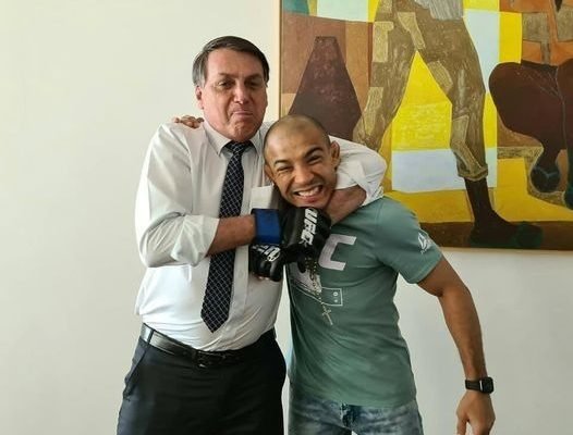O lutador José Aldo e o presidente Jair Bolsonaro posam para foto sorrindo, com o esportivo recebendo um "golpe" de brincadeira do mandatário - Metrópoles
