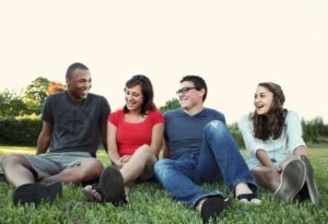Foto de grupo de quatro pessoas jovens rindo sentadas em grama - Metrópoles