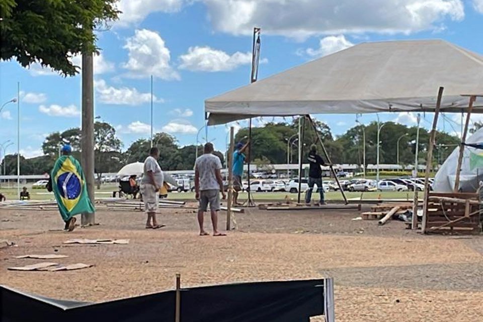 Acampamento bolsonarista no QG do Exército amanhece vazio, com estruturas desfeitas e lixo nas ruas após a posse do presidente Lula. No detalhe, homens desarmam toldo - Metrópoles