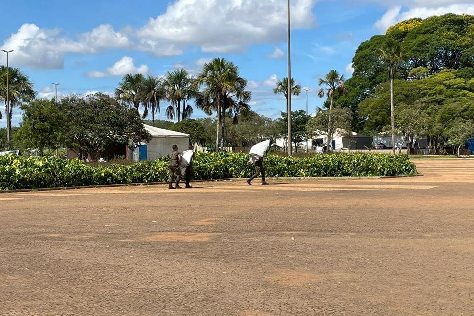 Acampamento bolsonarista no QG do Exército amanhece vazio, com estruturas desfeitas e lixo nas ruas após a posse do presidente Lula. No detalhe, homens desarmam toldo - Metrópoles