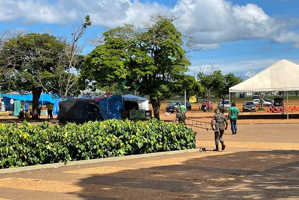 Acampamento bolsonarista no QG do Exército amanhece vazio, com estruturas desfeitas e lixo nas ruas após a posse do presidente Lula. No detalhe, homens desarmam toldo - Metrópoles