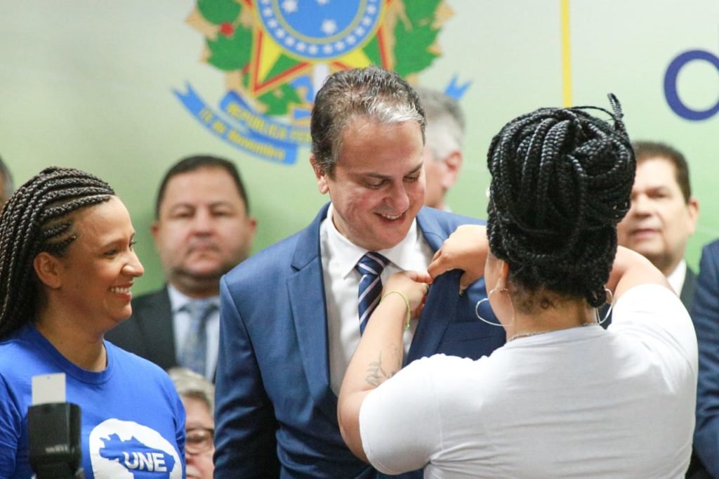 Camilo Santana toma posse como ministro da Educação em cerimônia no Ministério, cercado de autoridades e políticos, e recebe pin de ministro de duas alunas universitárias em cerimônia de posse - Metrópoles