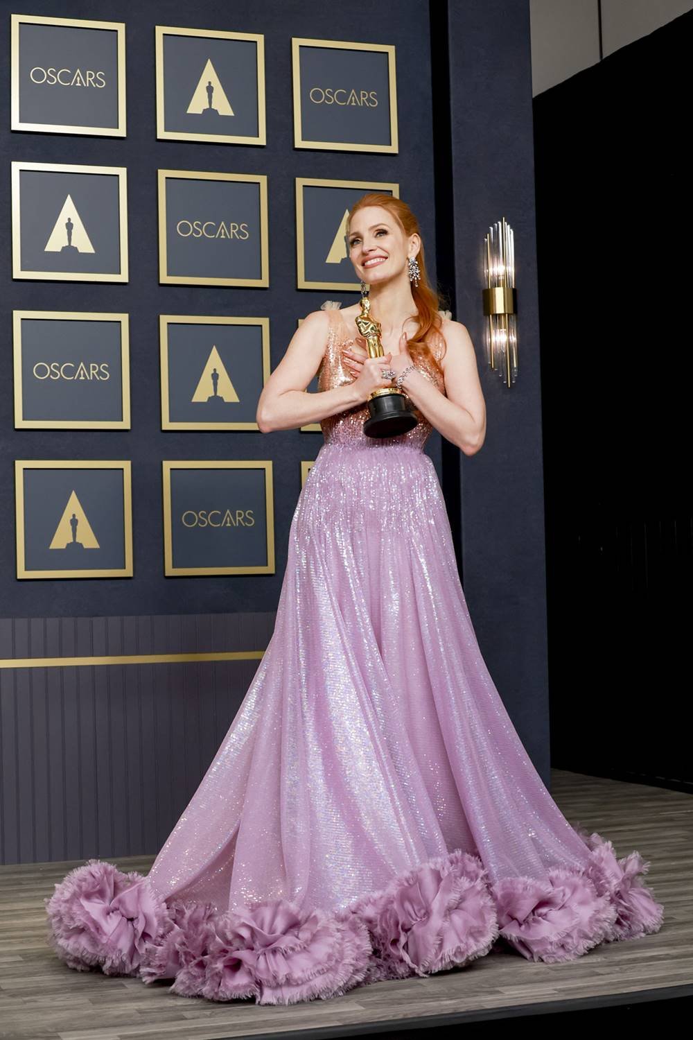 A atriz Jessica Chastain, uma mulher branca e jovem, de cabelo liso ruivo, posa para foto na festa do Oscar de 2022. Ela usa um vesrido da Gucci com brilho lilás. - Metrópoles