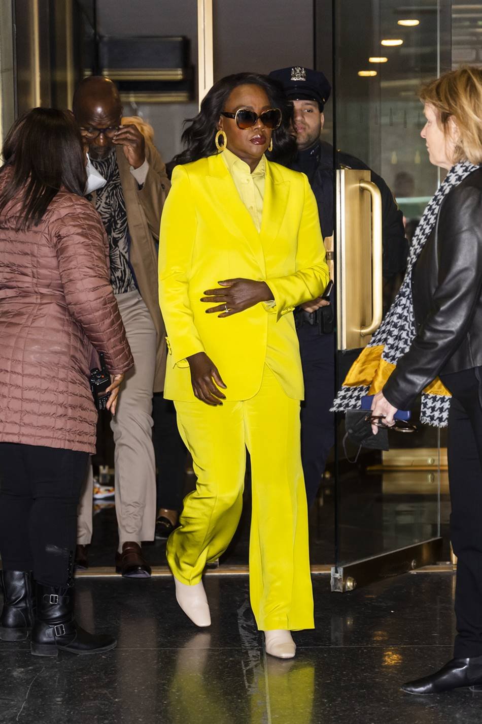A atriz Viola Davis, uma mulher negra e de meia idade, com cabelo ondulado preto, andando pela rua. Ela usa um look todo amarelo composto por: camisa de botão, calça social e blazer. Usa ainda óculos escuros e bota de couro branca . - Metrópoles