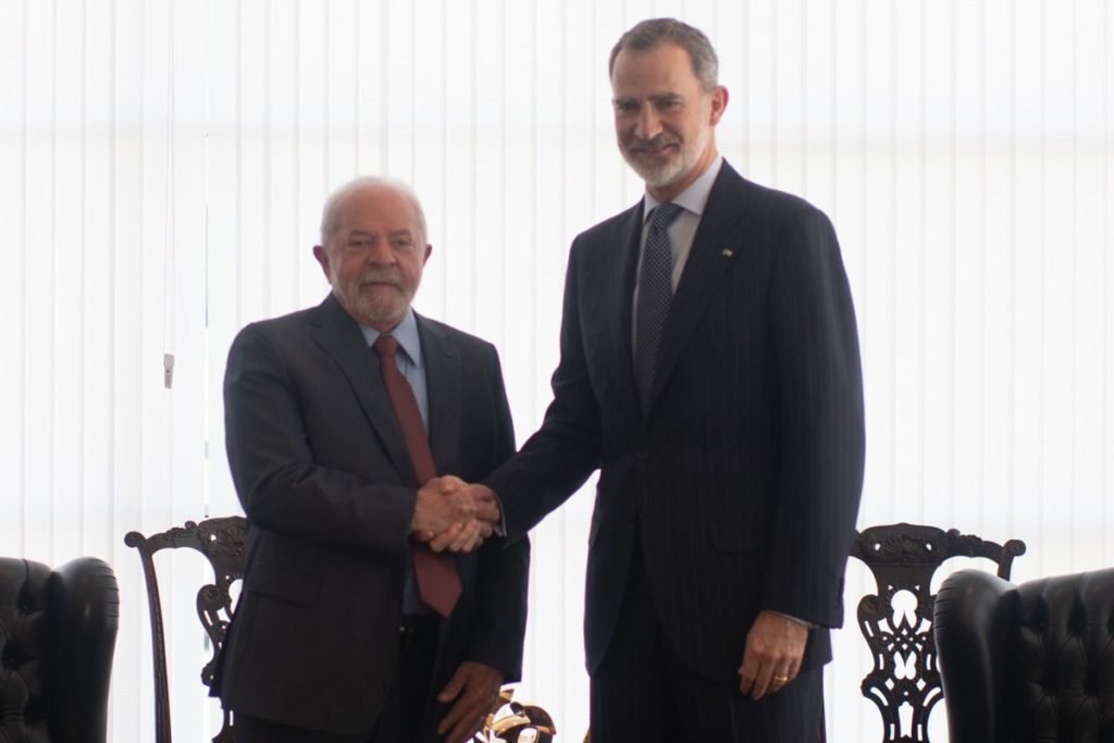 O rei da Espanha, Felipe IV, posa com Lula para foto enquanto apertam as mãos. Ambos sorriem - Metrópoles