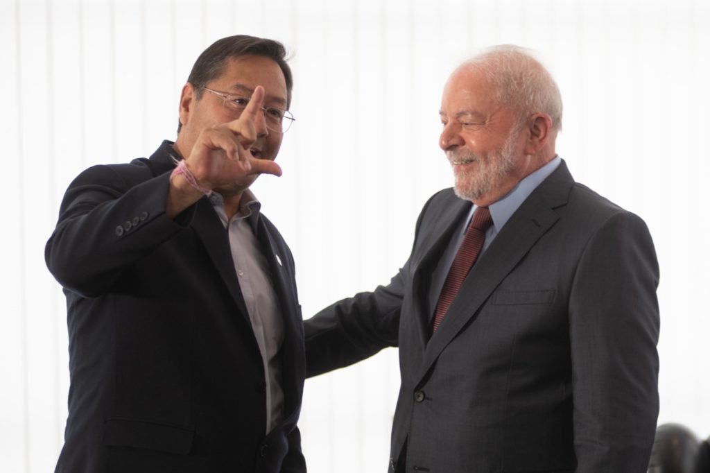 O presidente da Bolívia, Luis Arce, posa com Lula para foto enquanto apertam as mãos. Ambos sorriem e Arce