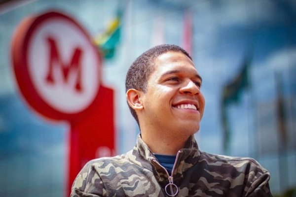 Fotografia de um homem negro sorrindo. Ao fundo, a logomarca da Faculdade Mackenzie.