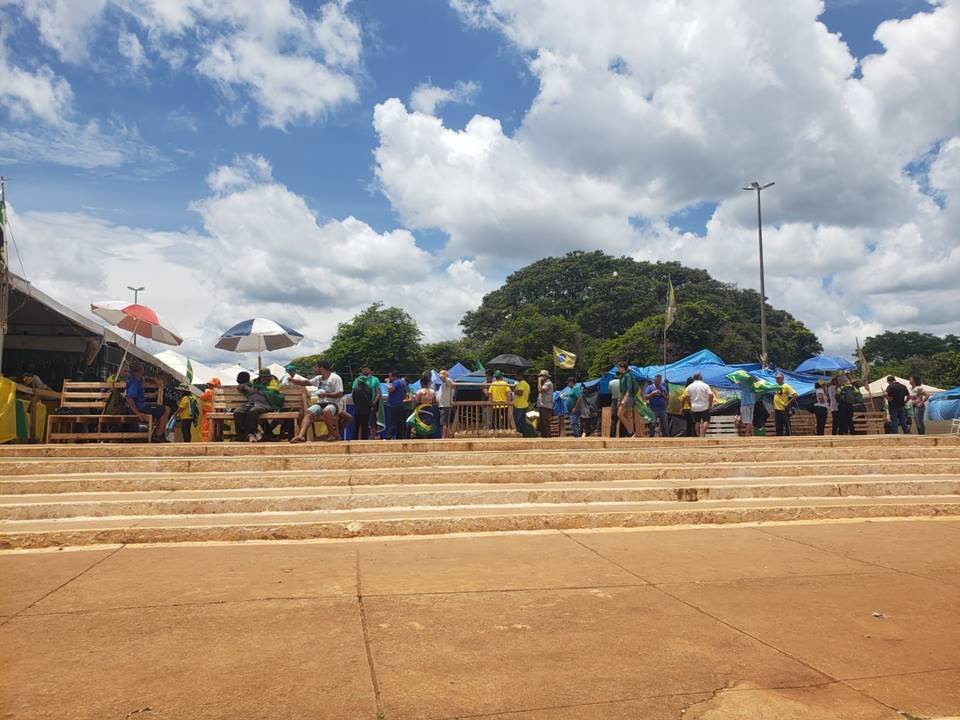Manifestantes bolsonaristas que resistem no acampamento do QG do Exército aparecem diante de escadaria sentados de baixo de tendas e segurando faixas - Metrópoles