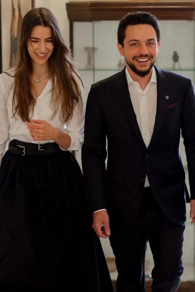 Foto colorida de mulher branca com blusa branca e saia preta ao lado de homem blazer - Metrópoles