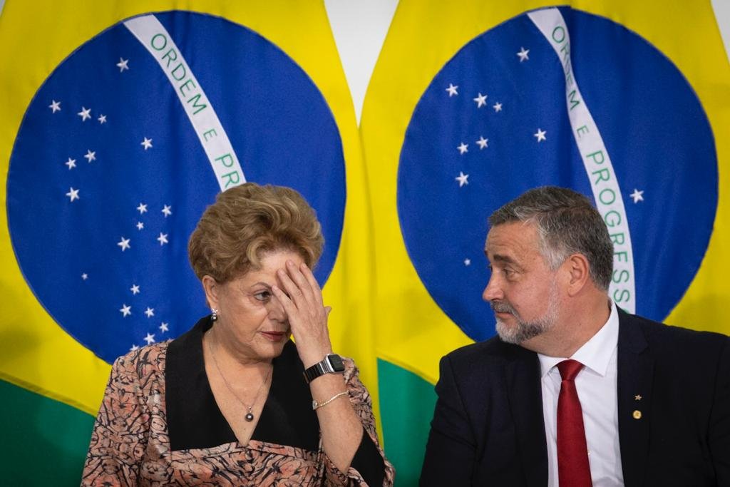 Paulo Pimenta toma posse como ministro de Estado Chefe da Secretaria de Comunicação da Presidência da República em cerimônia no palácio do Planalto. Ele conversa, sentado ao lado da ex-presidente Dilma Rousseff, com bandeiras do Brasil atrás - Metrópoles