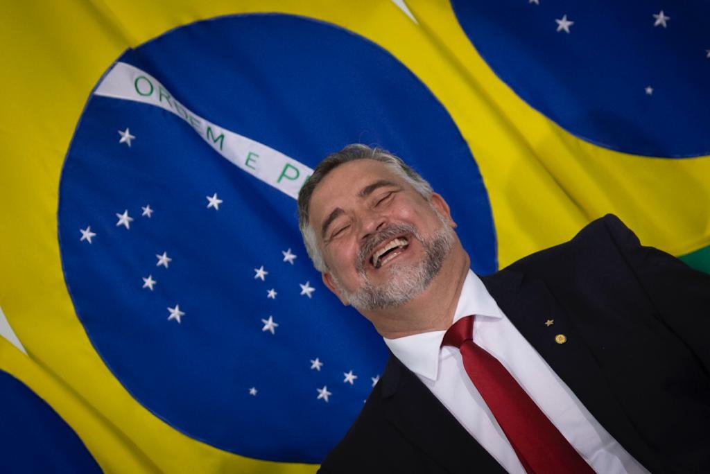 Ministro Paulo Pimenta da uma gargalhada ao lado da bandeira do Brasil - Metrópoles