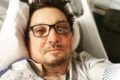 Jeremy Renner em uma cama de hospital. Ele usa óculos de grau e está com o rosto machucado - Metrópoles