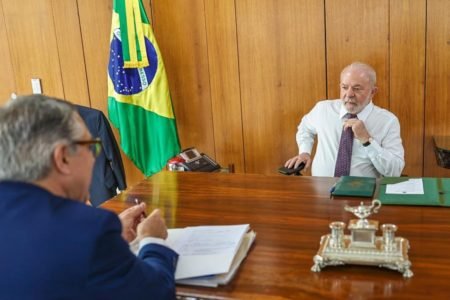 O presidente Lula conversa com seu ministro da Casa Civil, Alexandre Padilha, ambos sentados em uma mesa no Planalto. Ao fundo, a bandeira do Brasil - Metrópoles