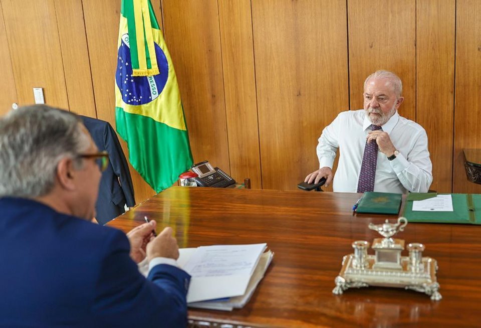 O presidente Lula conversa com seu ministro da Casa Civil, Alexandre Padilha, ambos sentados em uma mesa no Planalto. Ao fundo, a bandeira do Brasil - Metrópoles