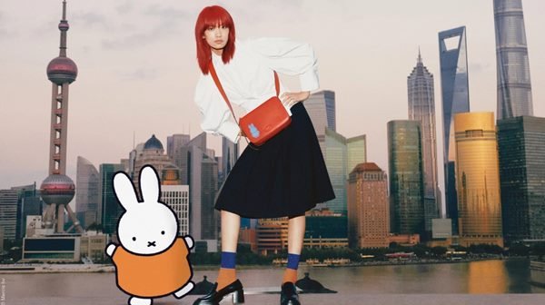 Mulher asiática em campanha de moda. Ela tem o cabelo vermelho e está posando com prédios ao fundo - Metrópoles