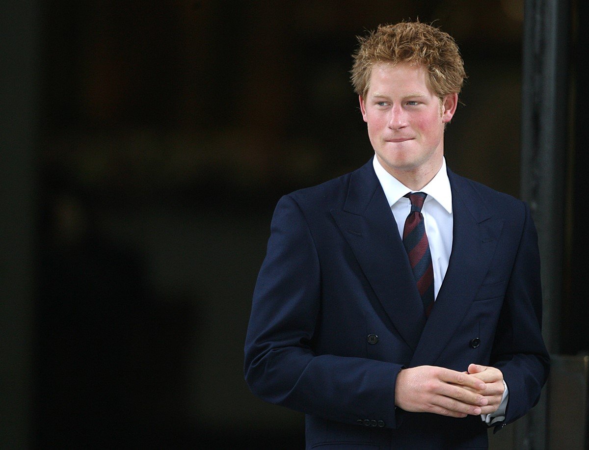 O príncipe Harry, um homem branco e jovem, de cabelo liso ruivo, posa para foto. Ele esta com uma camisa branca, um blazer azul e uma gravata bicolor azul e vinho. - Metrópoles