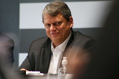 O governador de SP, Tarcísio de Freitas, sorri durante reunião. Ele aparece sentado em mesa - Metrópoles