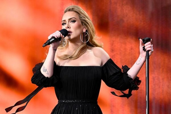 Cantora Adele durante performance segurando microfone com uma mão e pedestal na outra