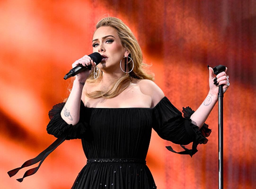 Cantora Adele durante performance segurando microfone com uma mão e pedestal na outra