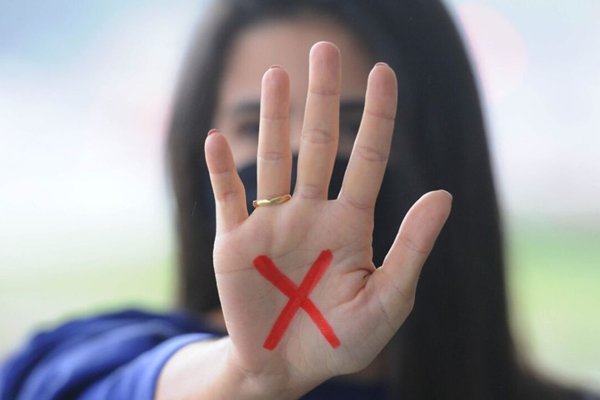 Fotografia de uma mulher mostrando a palma da mão com um x vermelho