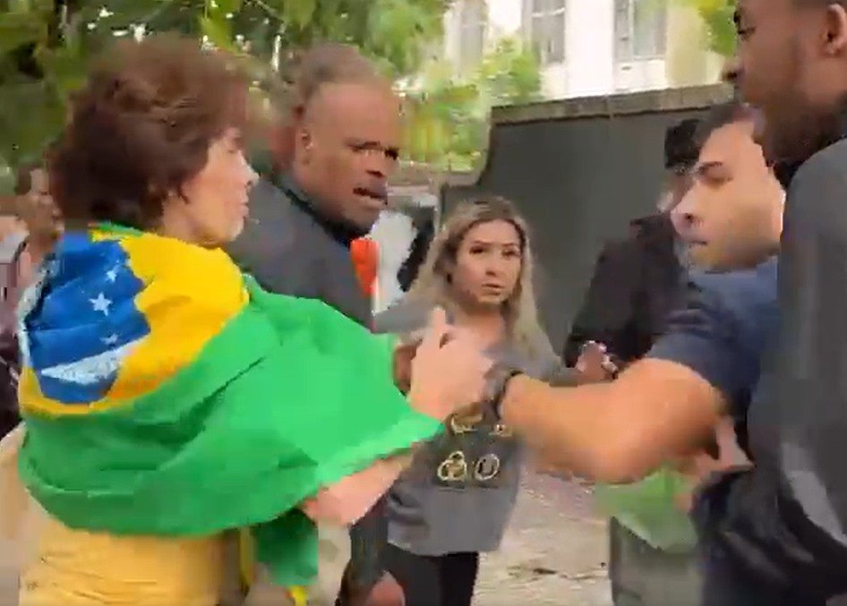 Jornalistas da Band são agredidos por militantes bolsonaristas e tem cozinhas quebradas em Belo Horizonte.  Na imagem, eles são cercados por vários homens e uma mulher com bandeira do Brasil ataca uma das câmeras - Metrópoles