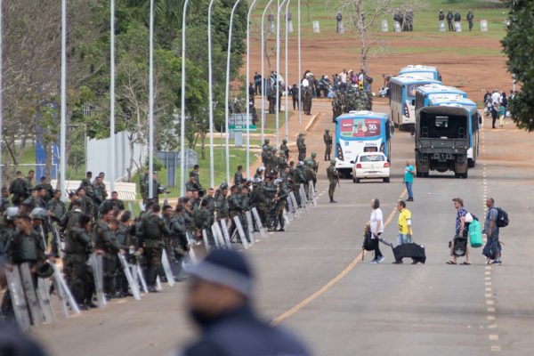 Agentes da PMDF e Exército desocupam acampamento bolsonarista no QG do Exército, em Brasília. Ao lado direito, percebe-se uma barreira de contenção de militares e ao fundo, vários ônibus levando detidos os terroristas que participaram da destruição da Esplanada - Metrópoles