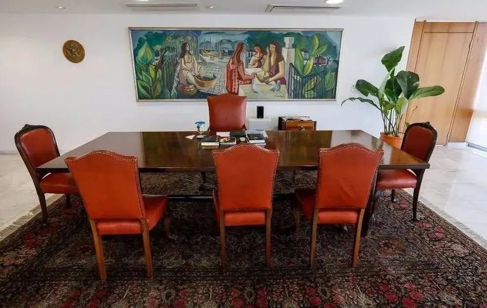 foto de sala com mesa de madeira com três cadeiras na frente, uma em cada ponta e uma na parte de trás e quadro na parede - metrópoles