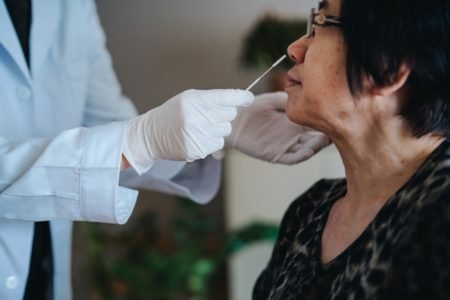 Imagem colorida de profissional da saúde fazendo swab nasal para teste de covid em idosa - Metrópoles