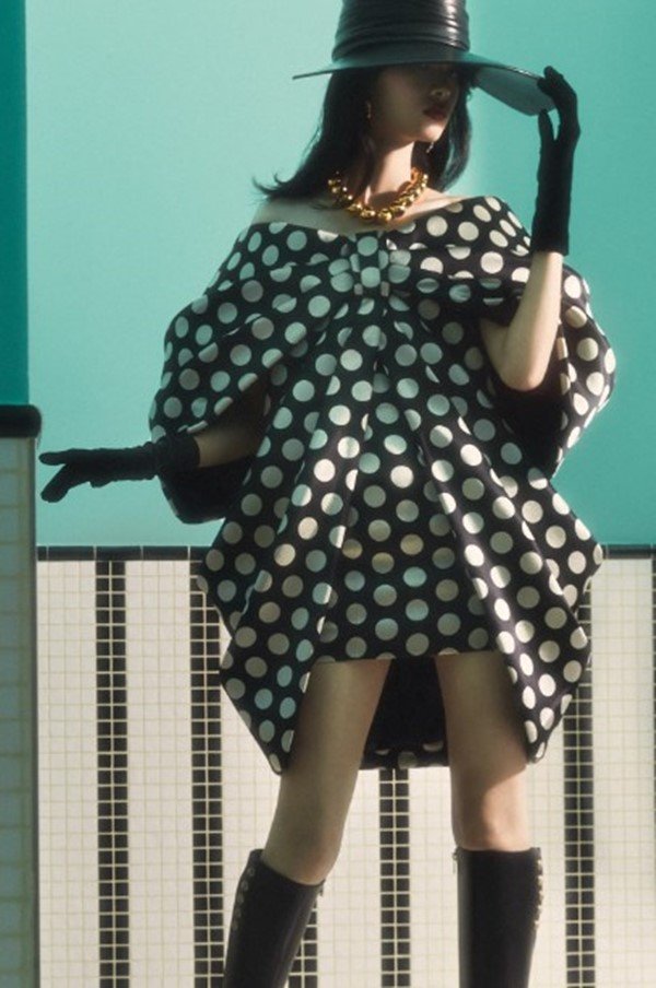 Mulher com roupas de outono em editorial de moda. Ela está posicionada em frente a uma parede azul - Metrópoles