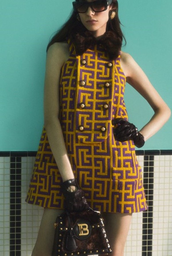 Mulher com roupas de outono em editorial de moda. Ela está posicionada em frente a uma parede azul - Metrópoles