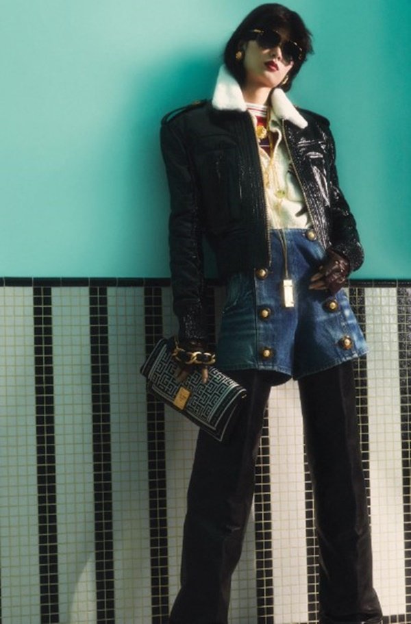 Mulher com roupas de outono em editorial de moda. Ela está posicionada em frente a uma parede azul - Metrópoles