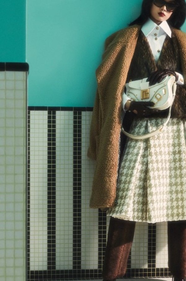 Mulher com roupas de outono em editorial de moda. Ela está posicionada em frente a uma parede azul - Metrópoles