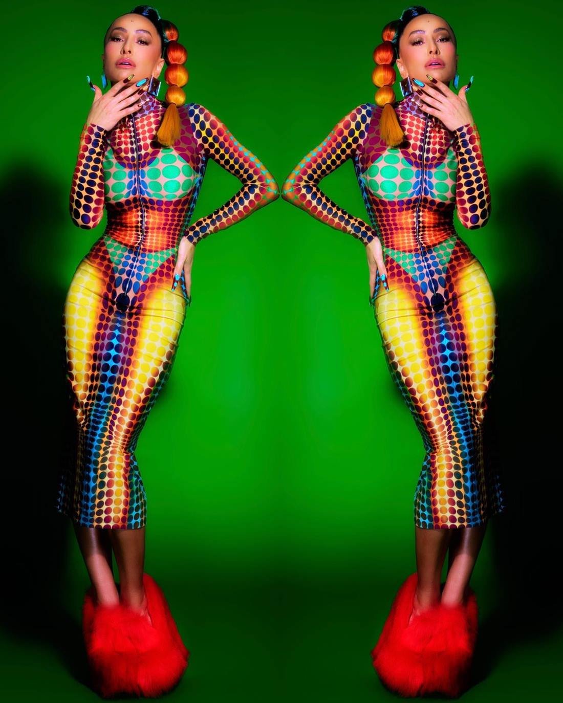 A ex-BBB e apresentadora Sabrina Sato, uma mulher jovem e morena, com traços asiáticos, posa para foto em um fundo verde. Ela usa uma peruca colorida e um vestido, também colorido, transparente da marca Jean Paul Gaultier. - Metrópoles