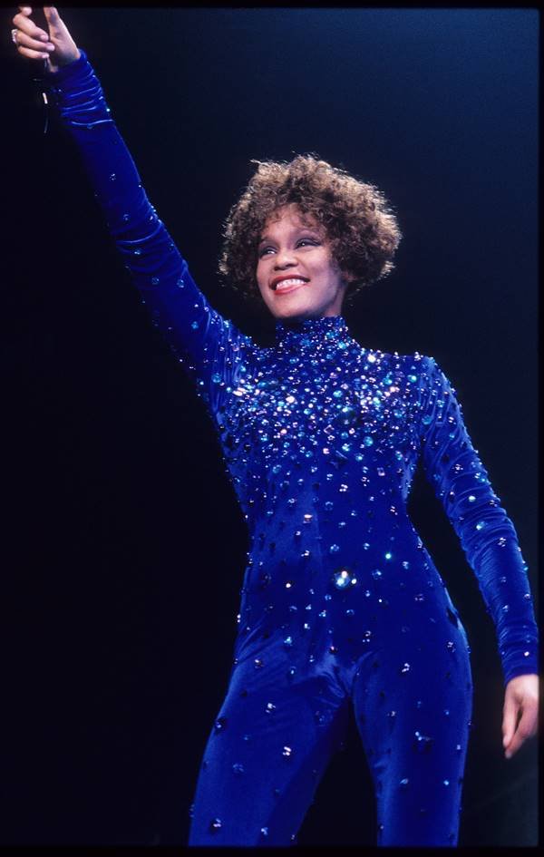 Whitney Houston usando macacão azul de gola alta e mangas compridas - Metrópoles