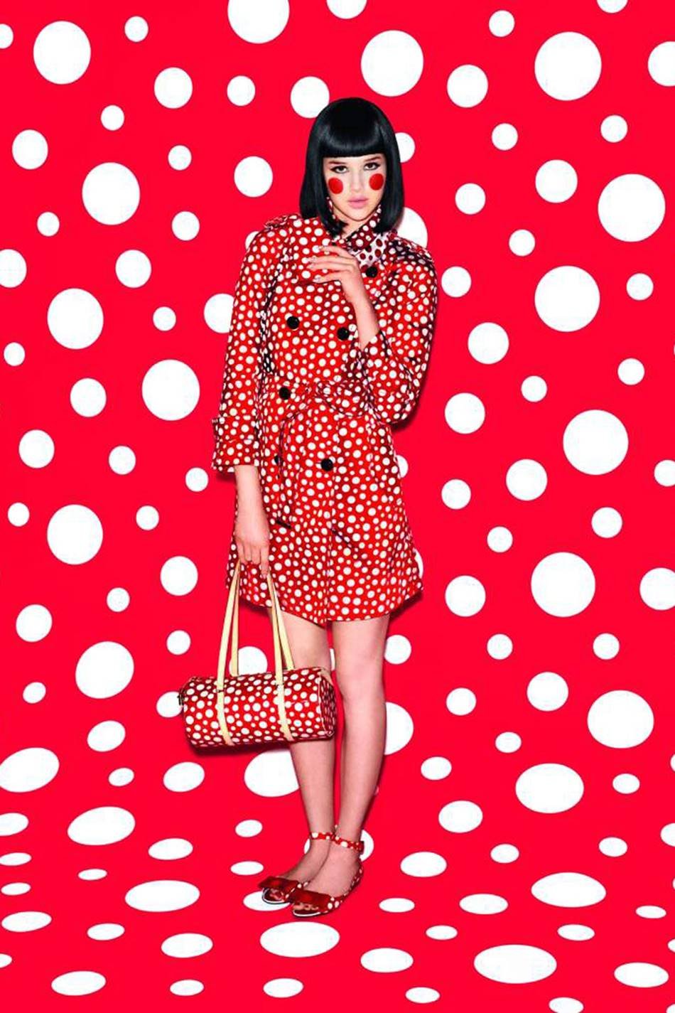 Foto de campanha publicitária da marca Louis Vuitton. A coleção de roupas e acessórios foi feita em parceria com a artista Yayoi Kusama. A modelo, branca e jovem, de cabelo curto chanel preto, usa um vestido vermelho com bolas brancas e uma bolsa de couro c om a mesma estampa. - Metrópoles