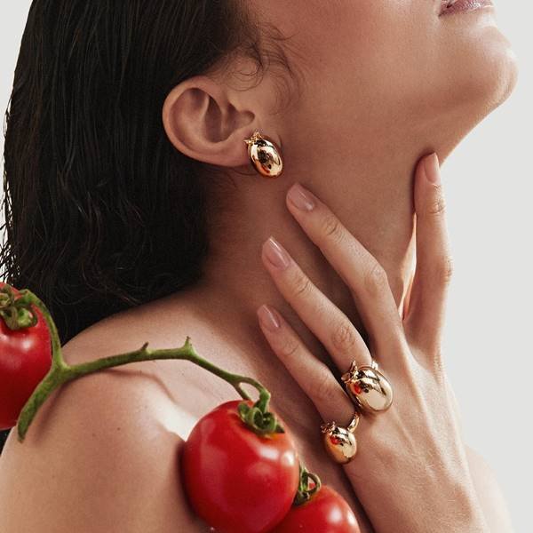 Mulher usa peças douradas da marca Abi Project e tem tomates posicionados em seu ombro - Metrópoles