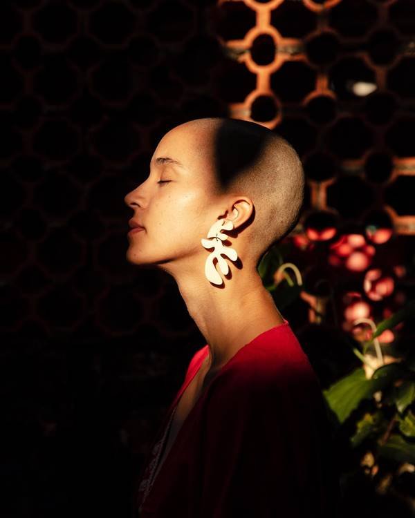 Modelo careca em foto de perfil com sombra sob o rosto usa brinco branco em forma de folhas da marca Azulerde - Metrópoles