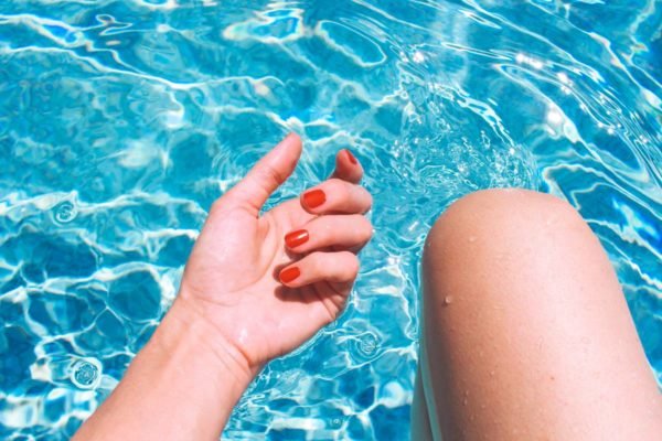 Mão de uma mulher branca com unhas vermelhas, na piscina. - Metrópoles